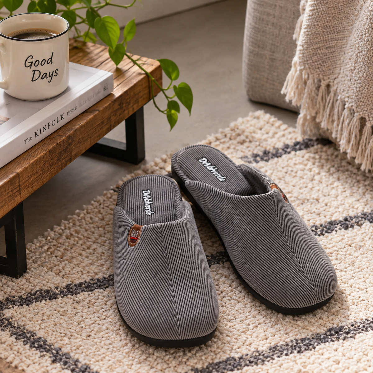 Zapatillas de hogar para hombre en gris, sobre alfombra junto a mesa de madera y taza de café.