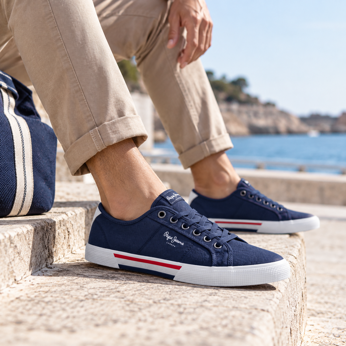 Zapatillas de lona para hombre en color azul marino, combinadas con pantalón beige en un entorno costero.