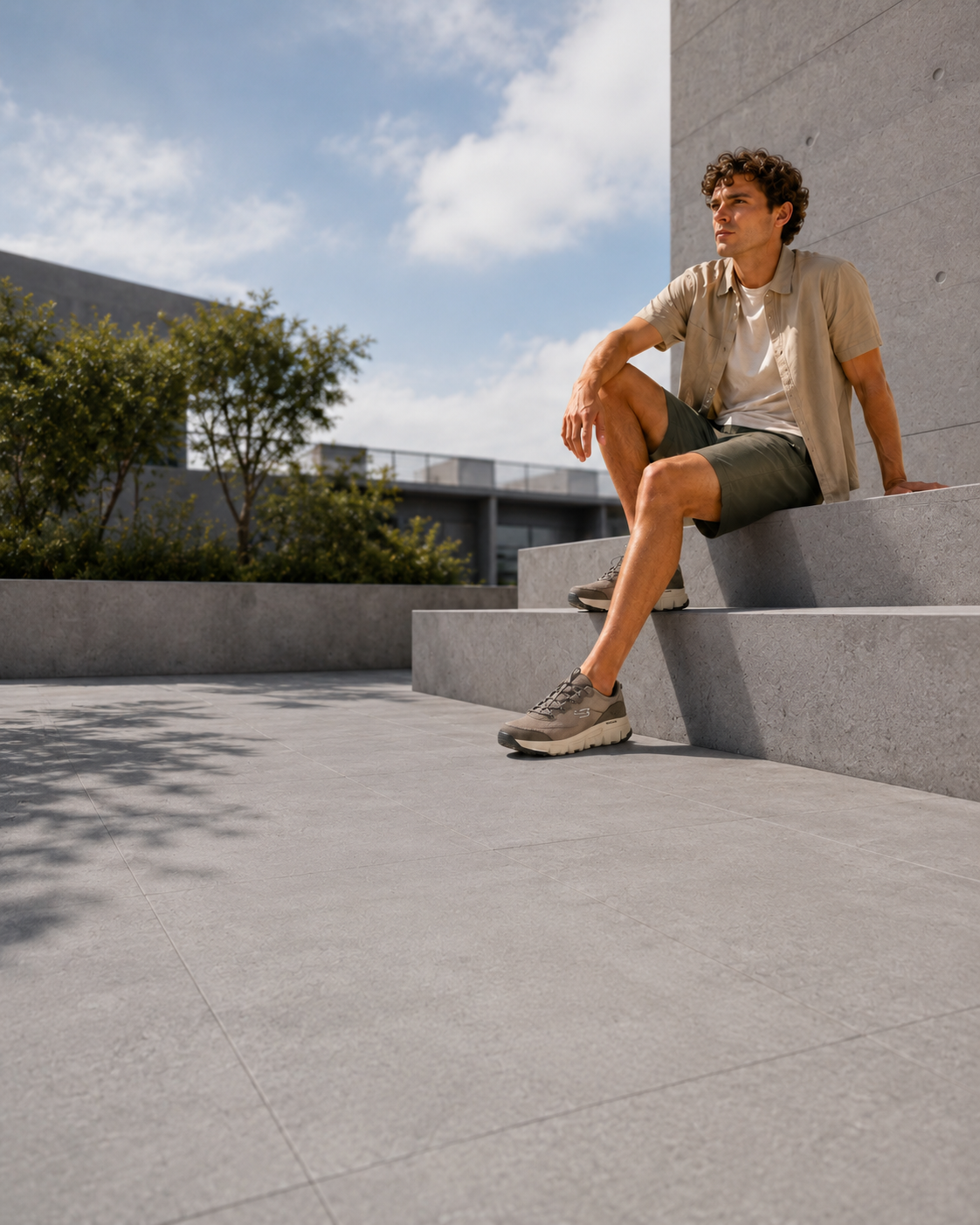 Hombre con zapatillas Skechers sentado en un entorno exterior de arquitectura minimalista